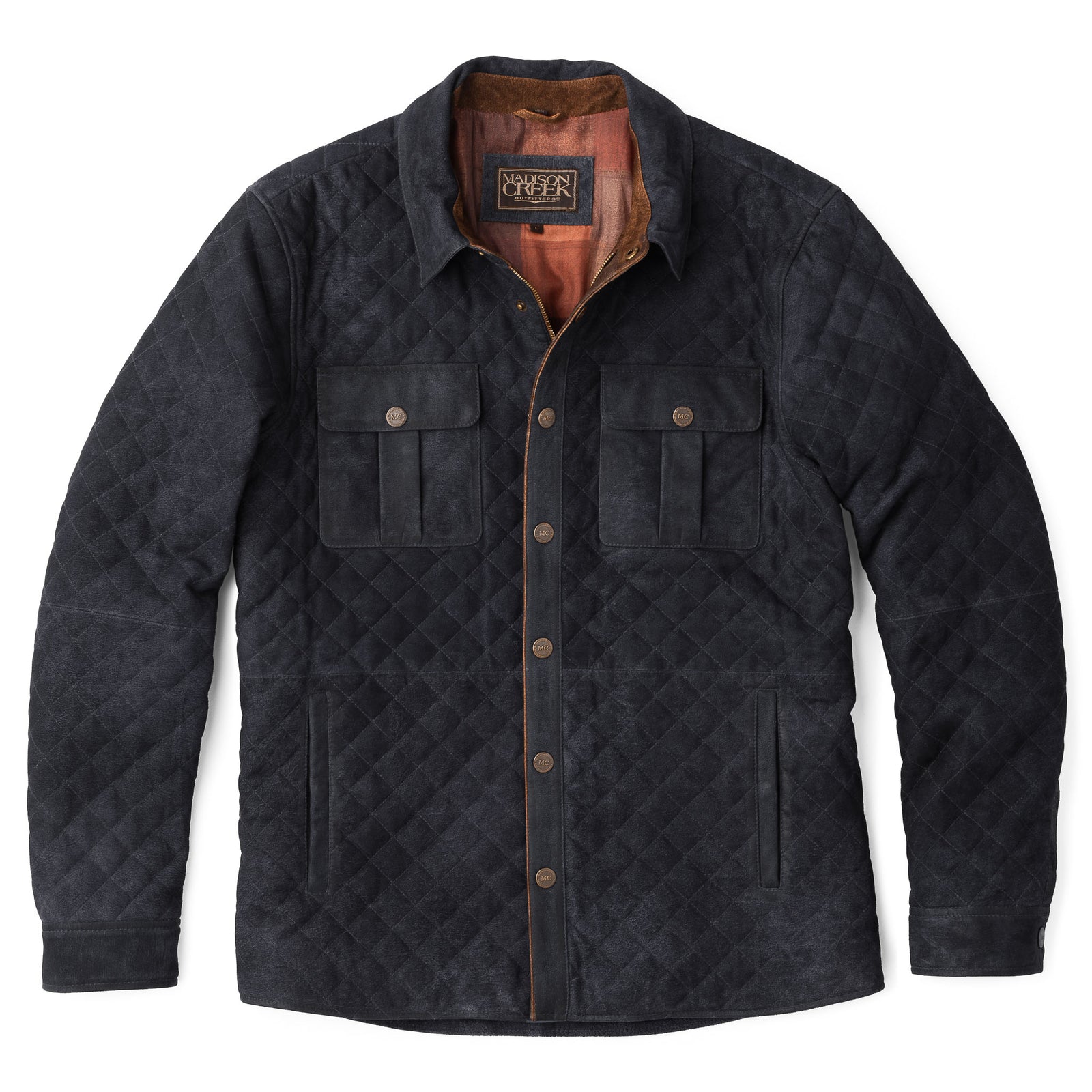 Model wearing the men’s Franklin Waxed Goat Suede Quilted Jacket in Navy, unsnapped over a plaid shirt to reveal the contrast suede trim, standing outdoors with city buildings in the background.