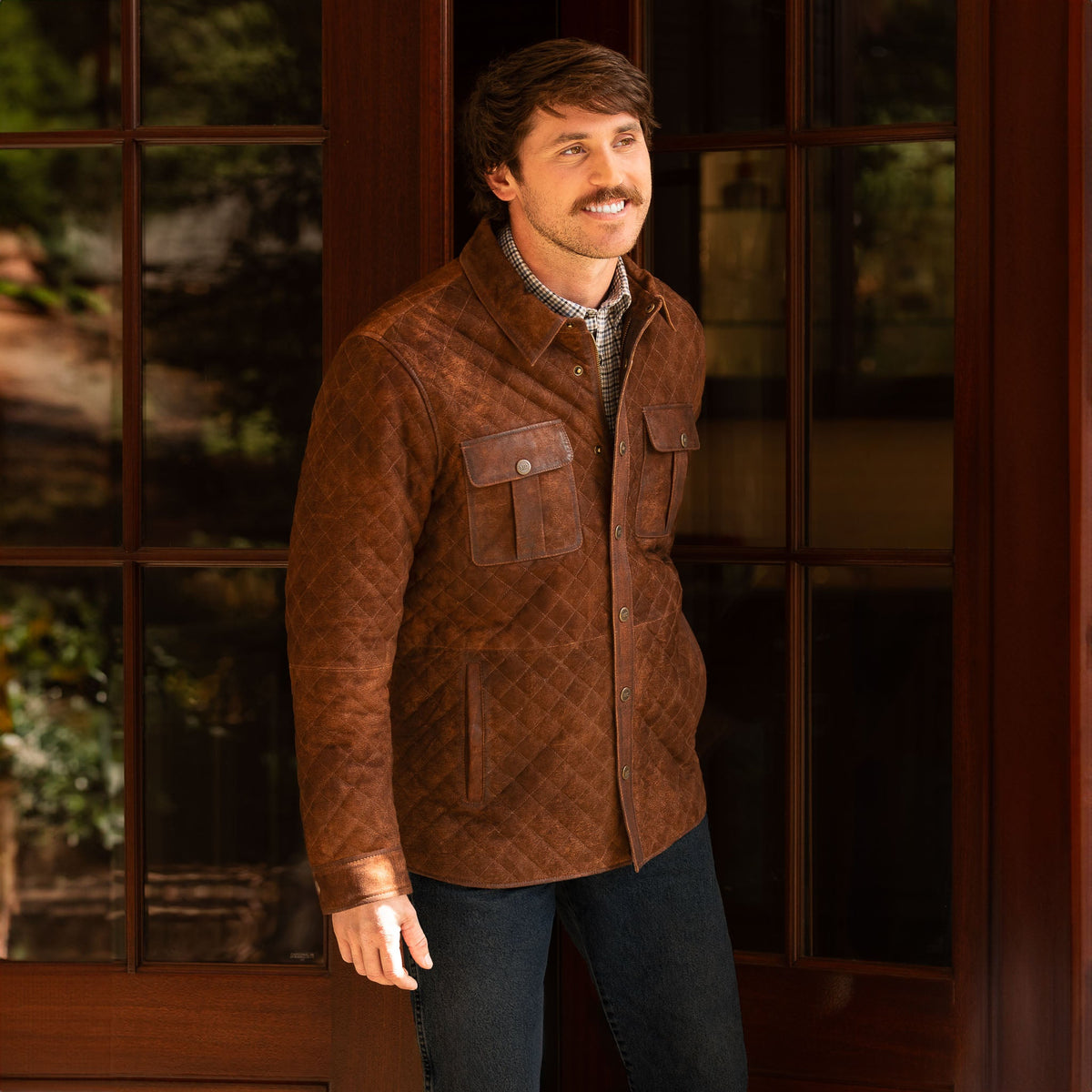 Model wearing the men‚Äôs Franklin Waxed Goat Suede Quilted Jacket in Bourbon, snapped closed with pleated chest pockets and quilted suede body.